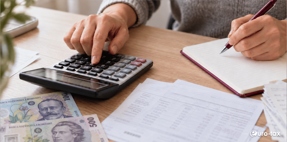 Calcularea impozitului pe venit, cu documente financiare, calculator și bancnote românești pe birou.